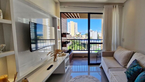 A modern living room with a flat-screen TV, a sofa, and a balcony with a city view.