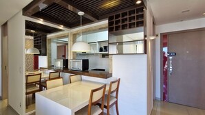 A modern kitchen with a dining area, featuring a white table and chairs, a built-in oven, and pendant lighting.
