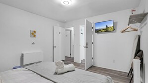 Une chambre d’hôtel avec un lit, un téléviseur fixé au mur et une porte donnant sur une autre pièce.