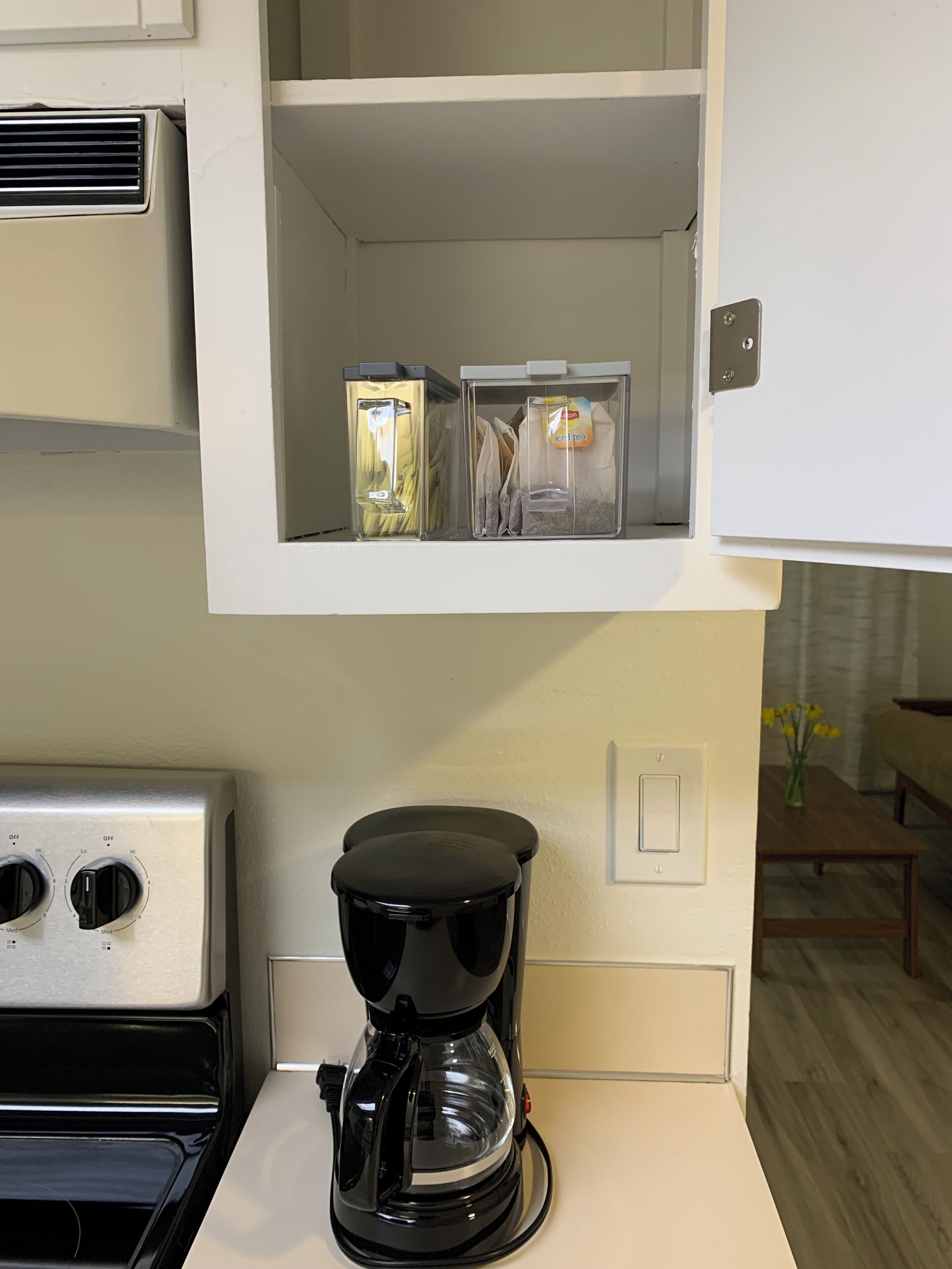 A kitchen with a coffee maker, a microwave, and two clear storage containers on a shelf.