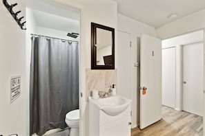 A bathroom with a shower curtain, a sink with a mirror, and a toilet. - Central Bellevue Guesthouse  (Bellevue)