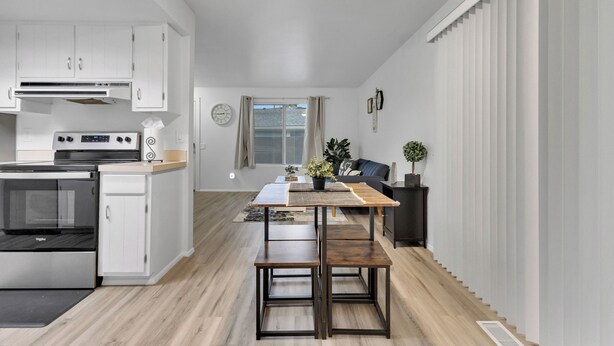 Une cuisine moderne avec des armoires blanches, un four encastré et un coin repas comprenant une table et des bancs en bois.