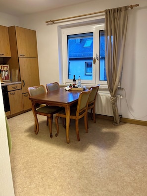 A dining area with a wooden table and chairs, a window with curtains, and a wooden cabinet with knives. - Cozy and quiet apartment in Rosenthal am Rennsteig (OT Blankenstein) (Rosenthal am Rennsteig)