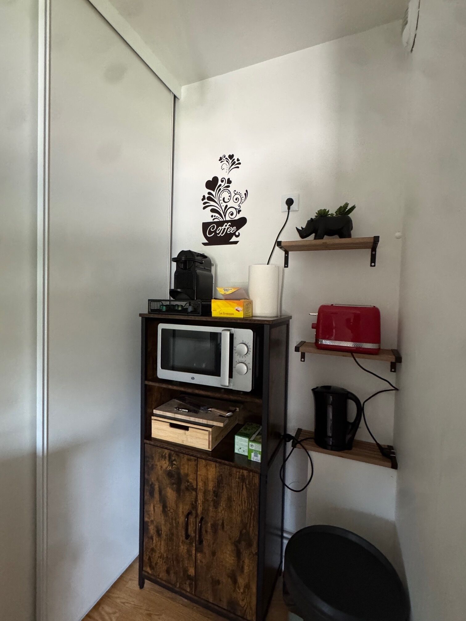 A compact kitchenette with a microwave, coffee machine, and a small shelf with a red toaster.