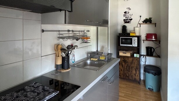 A modern kitchen with grey cabinets, a stainless steel sink, and a built-in oven. There is a wooden cabinet with a microwave and a kettle on the countertop. - Apartment ideally located, Beach / Motorway / Shops / Hospital / Railway station... (Verton)