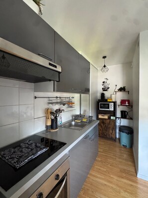 A modern kitchen with grey cabinets, a stainless steel sink, and a built-in oven. There is a wooden cabinet with a microwave and a kettle on the countertop. - Apartment ideally located, Beach / Motorway / Shops / Hospital / Railway station... (Verton)