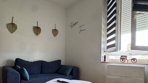 A modern living room with a blue sofa, a white coffee table, and a small white ottoman. There are decorative wall hangings and a window with blinds. - Apartment ideally located, Beach / Motorway / Shops / Hospital / Railway station... (Verton)
