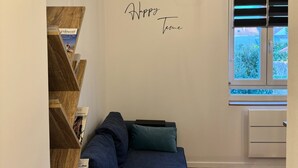 A room with a dark blue sofa, a wooden bookshelf, and a window with blinds. - Apartment ideally located, Beach / Motorway / Shops / Hospital / Railway station... (Verton)