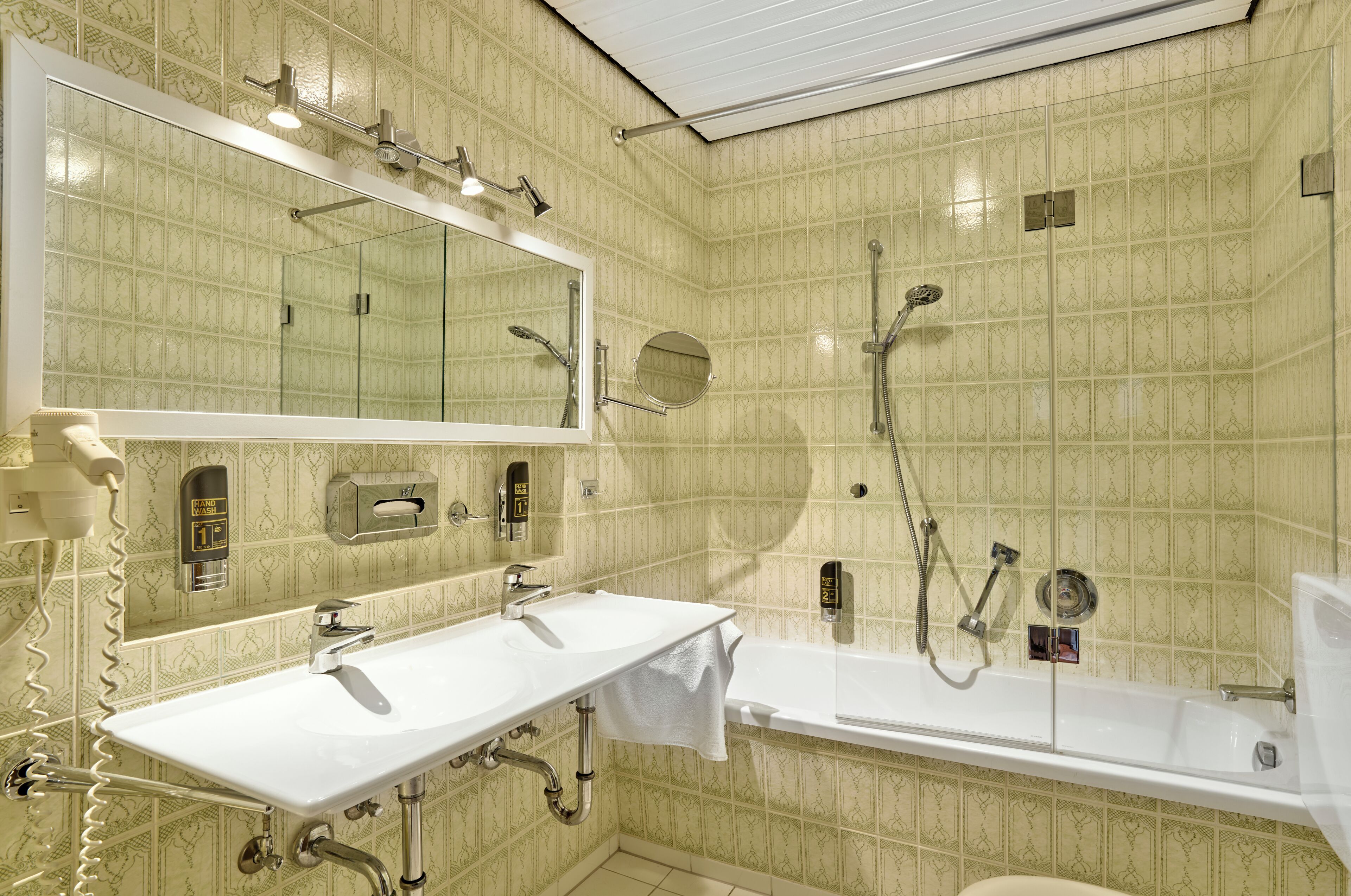 Un baño con lavamanos doble, un espejo grande, ducha y retrete.