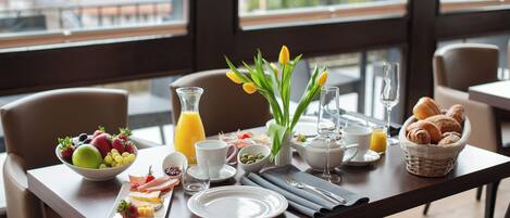 Ein Frühstückstisch, gedeckt mit einer Obstschale, Croissants und einer Tulpenvase.