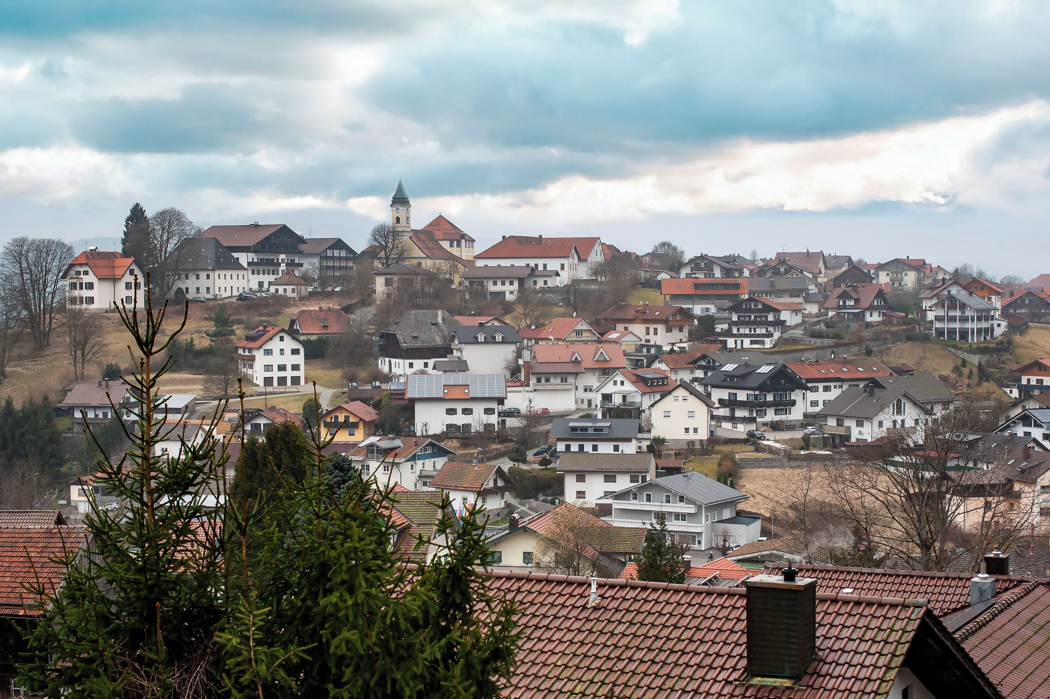 A residential area with houses, a church tower, and a hill.