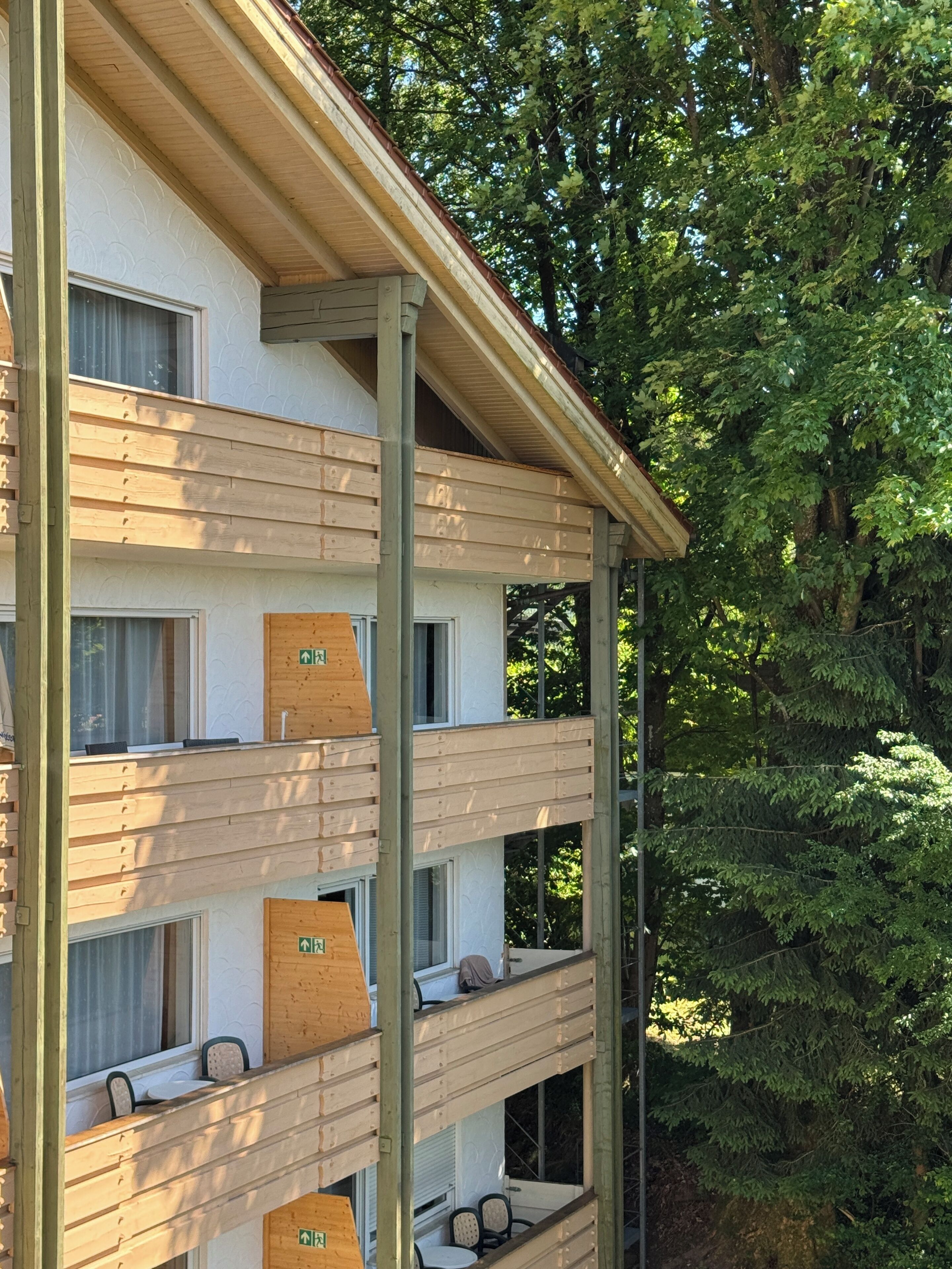 A multi-story building with a wooden facade, multiple balconies, and a view of surrounding trees.