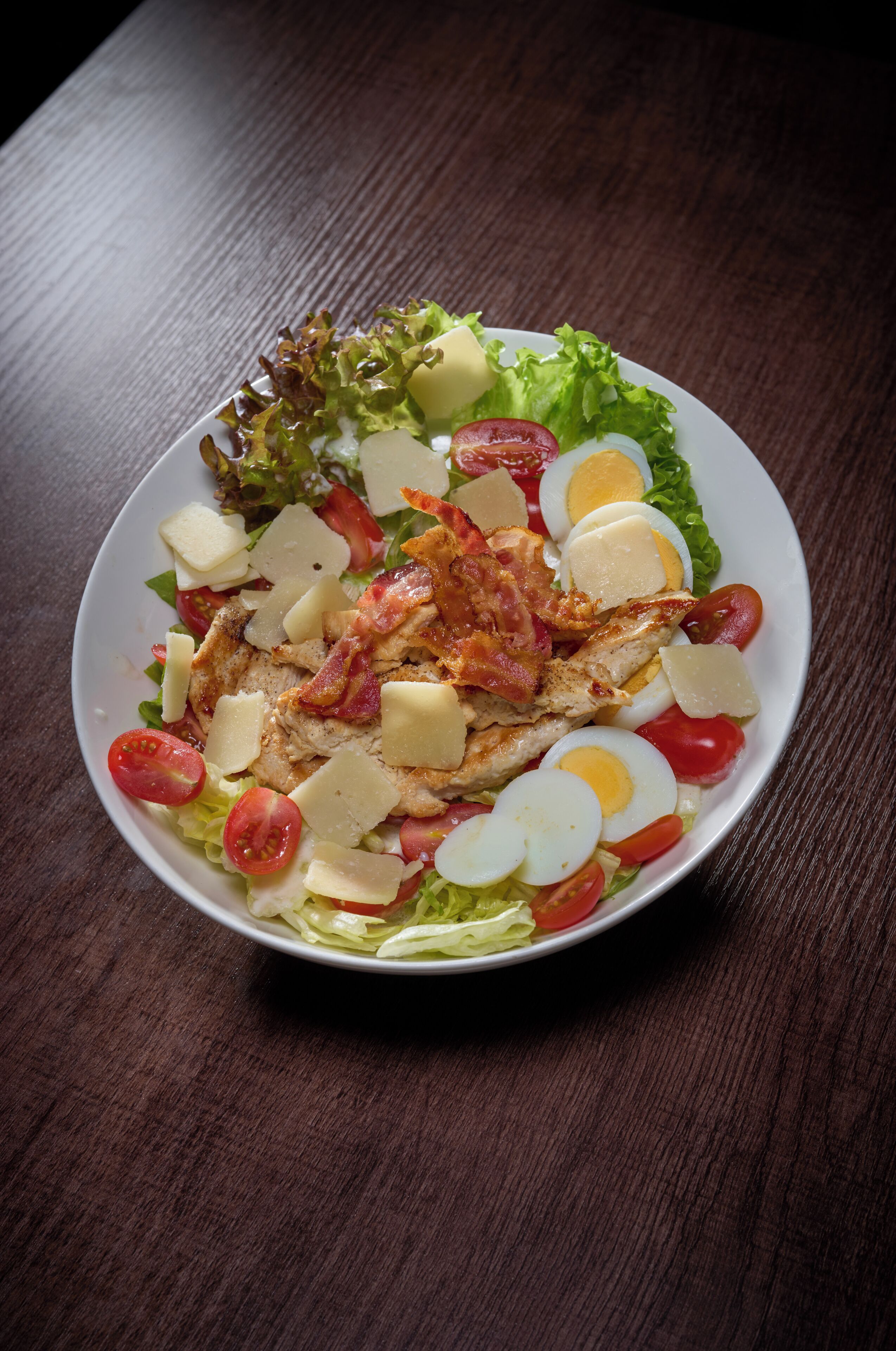 A salad with lettuce, tomatoes, cheese, and eggs on a white plate.