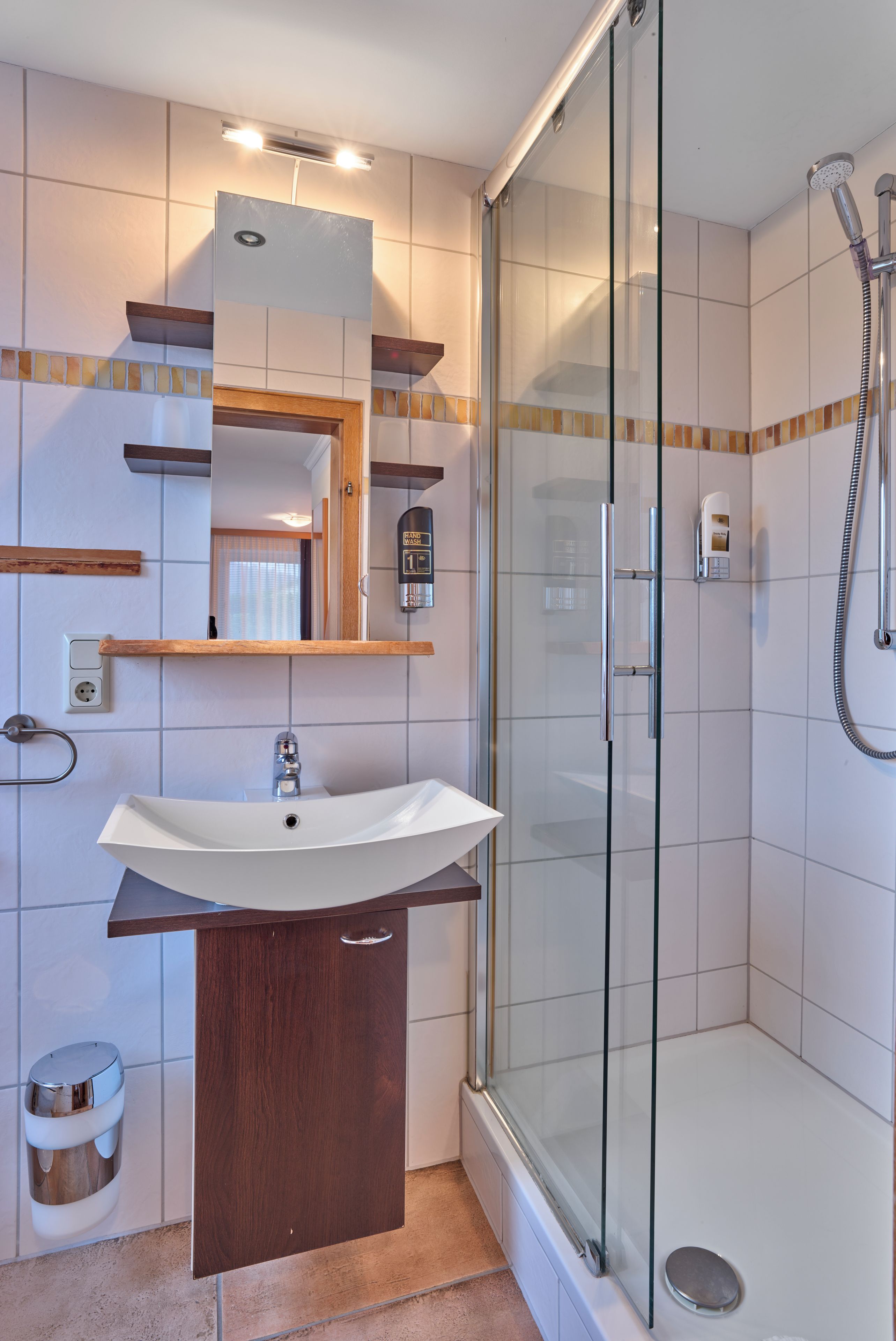 A modern bathroom with a glass shower enclosure, a built-in sink, and a hand wash station.
