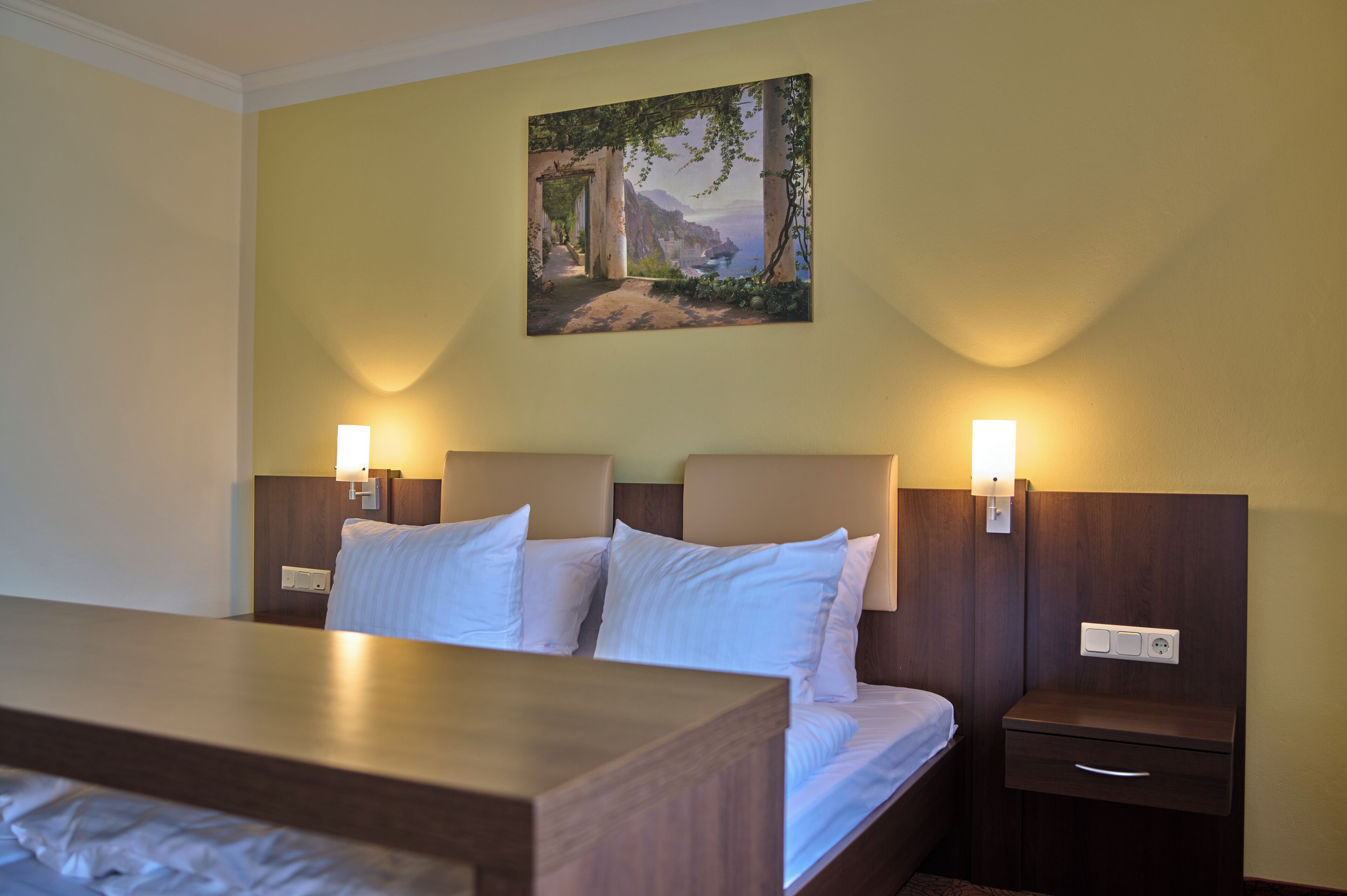 Een hotelkamer met een bed, nachtkastjes en een schilderij aan de muur.