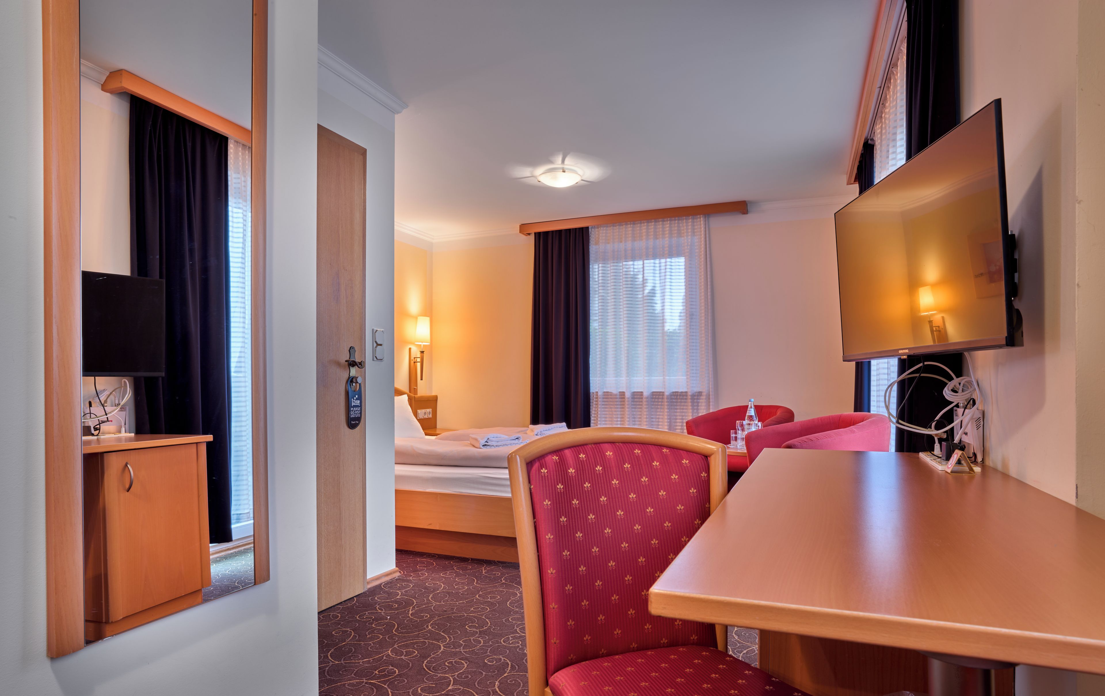Een hotelkamer met een bed, een bureau, een stoel, een televisie en een deur.