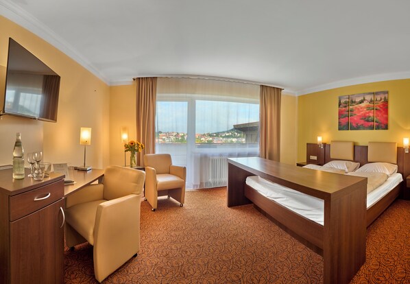 A hotel room with a bed, a desk, a chair, a TV, and a window with a city view. - LuCA HOTEL (Bodenmais)