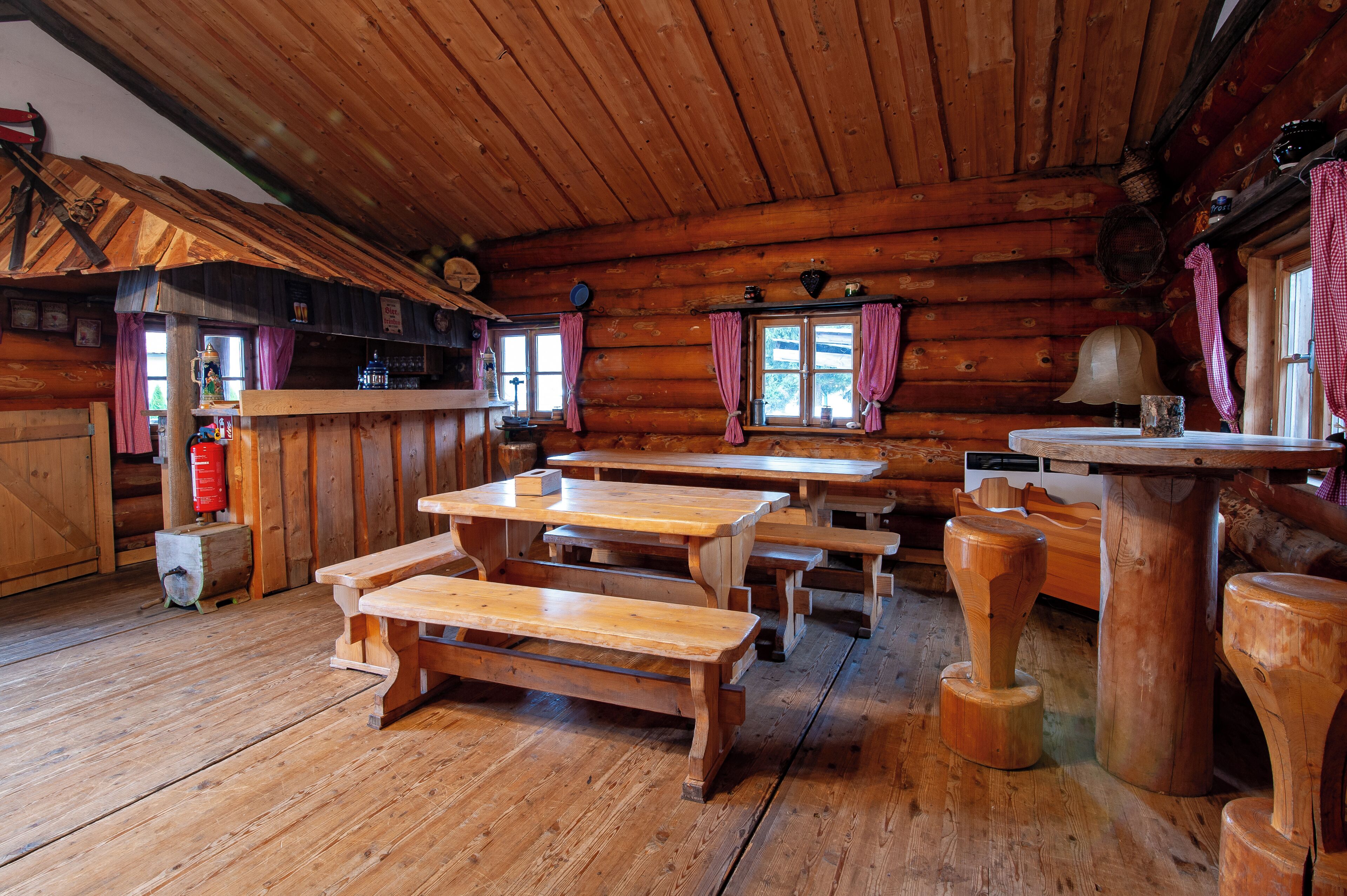 Una cabaña rústica de madera con mesas y bancos de madera, una zona de bar y una chimenea.