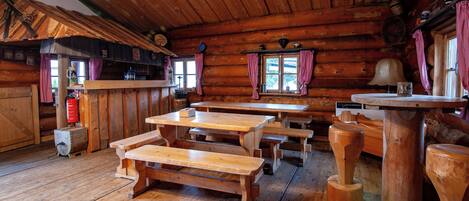 Una cabaña rústica de madera con mesas y bancos de madera, una zona de bar y una chimenea.