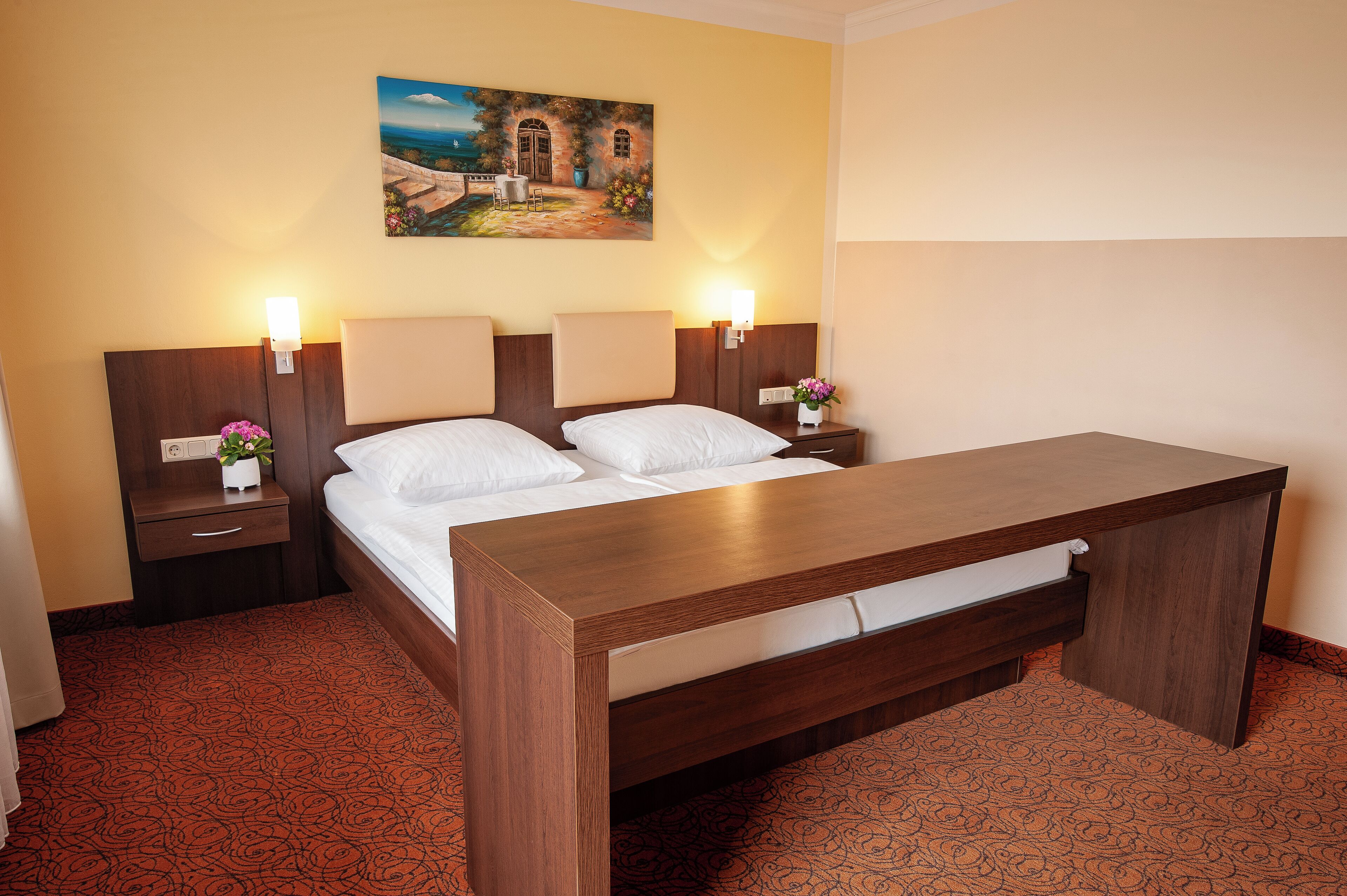 A hotel room with a bed, two bedside tables, a nightstand, a desk, and a painting on the wall.