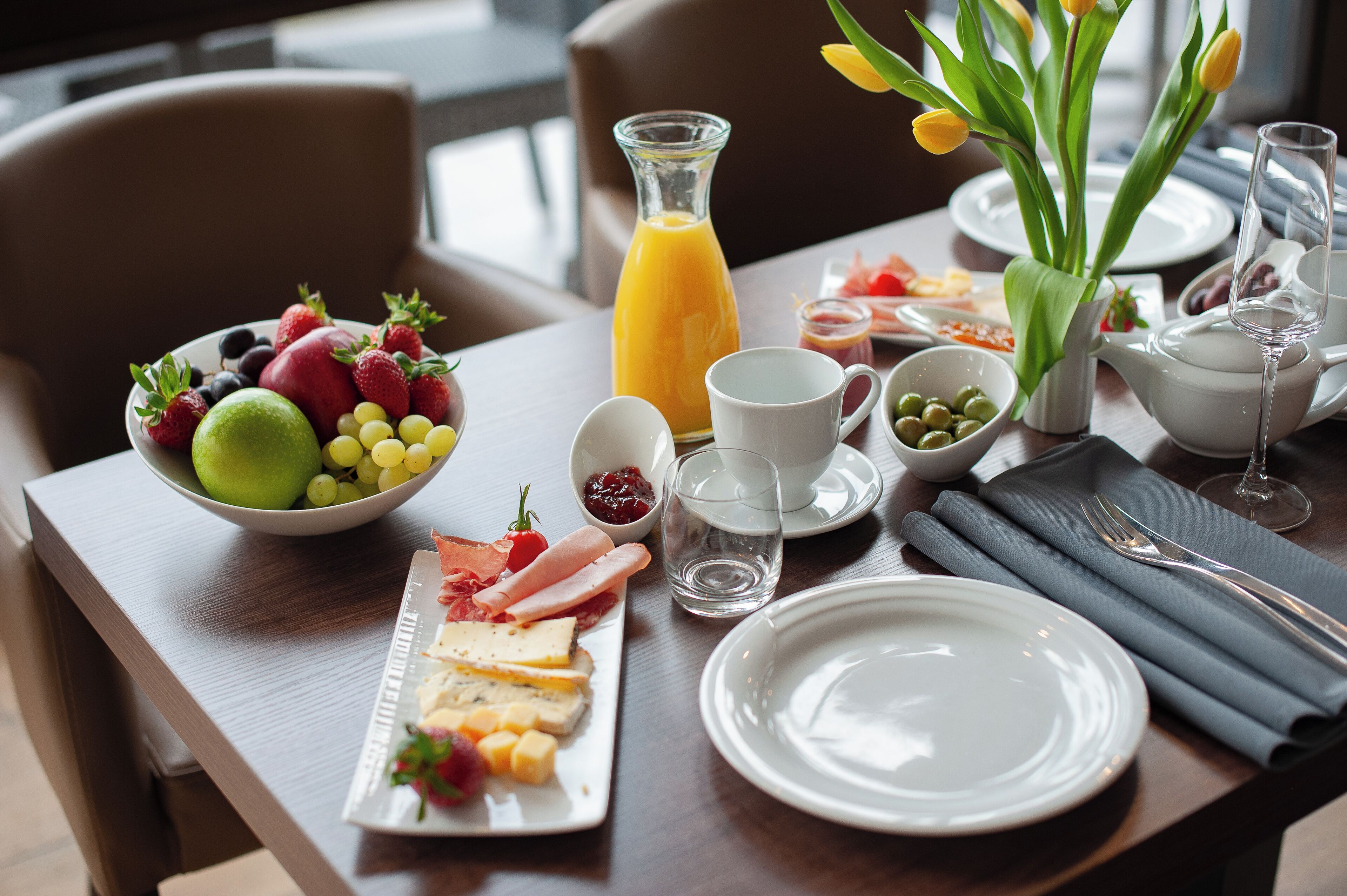 A breakfast setting with a fruit bowl, cheese platter, and a pitcher of orange juice.