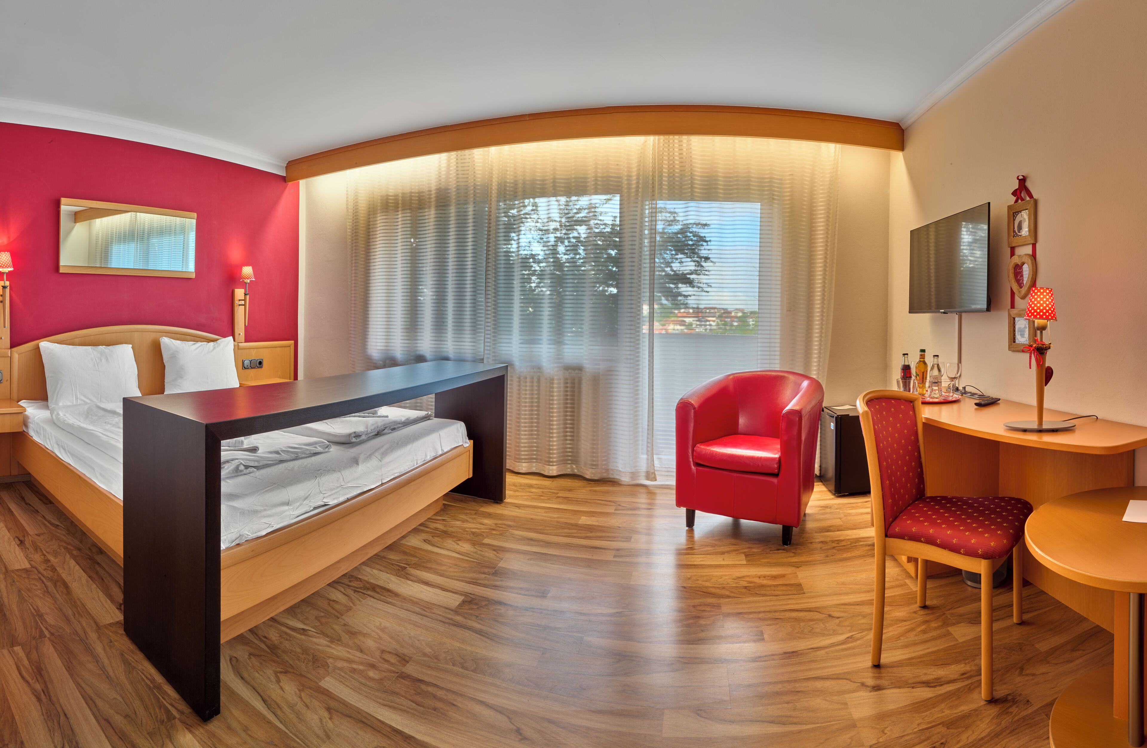Una habitación de hotel moderna con una cama, un escritorio, una silla, un televisor y un ventanal con cortinas.