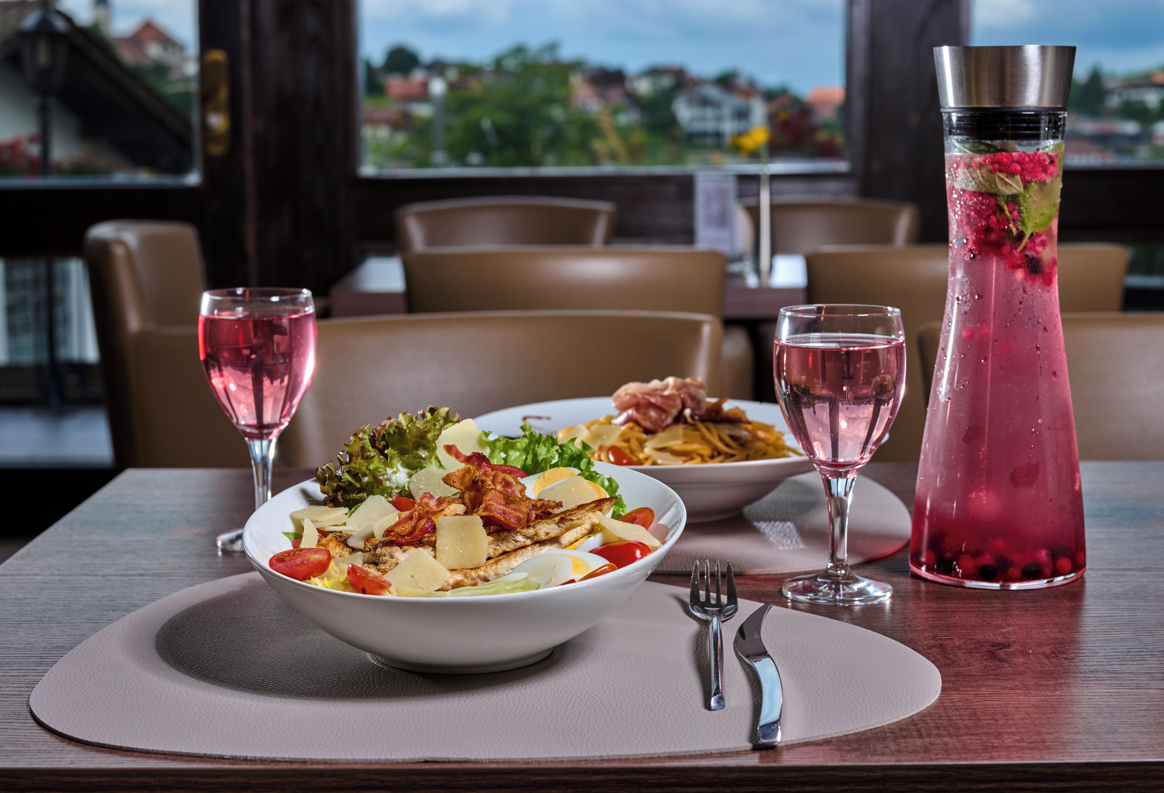 A dining table with a meal, two glasses of pink drink, and a tall glass with a floral garnish.