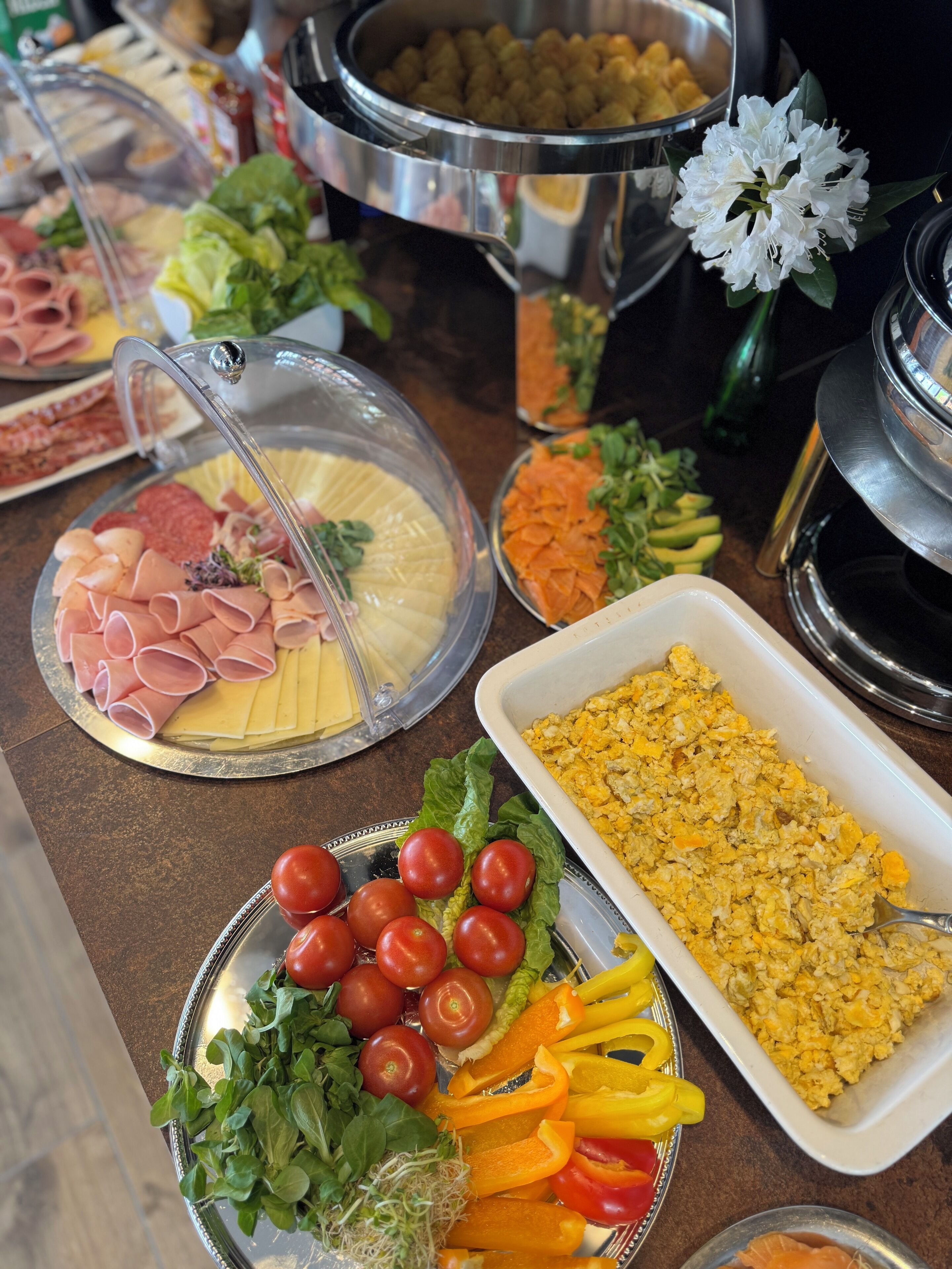 A buffet table with various food items including meats, cheeses, vegetables, and a casserole dish.