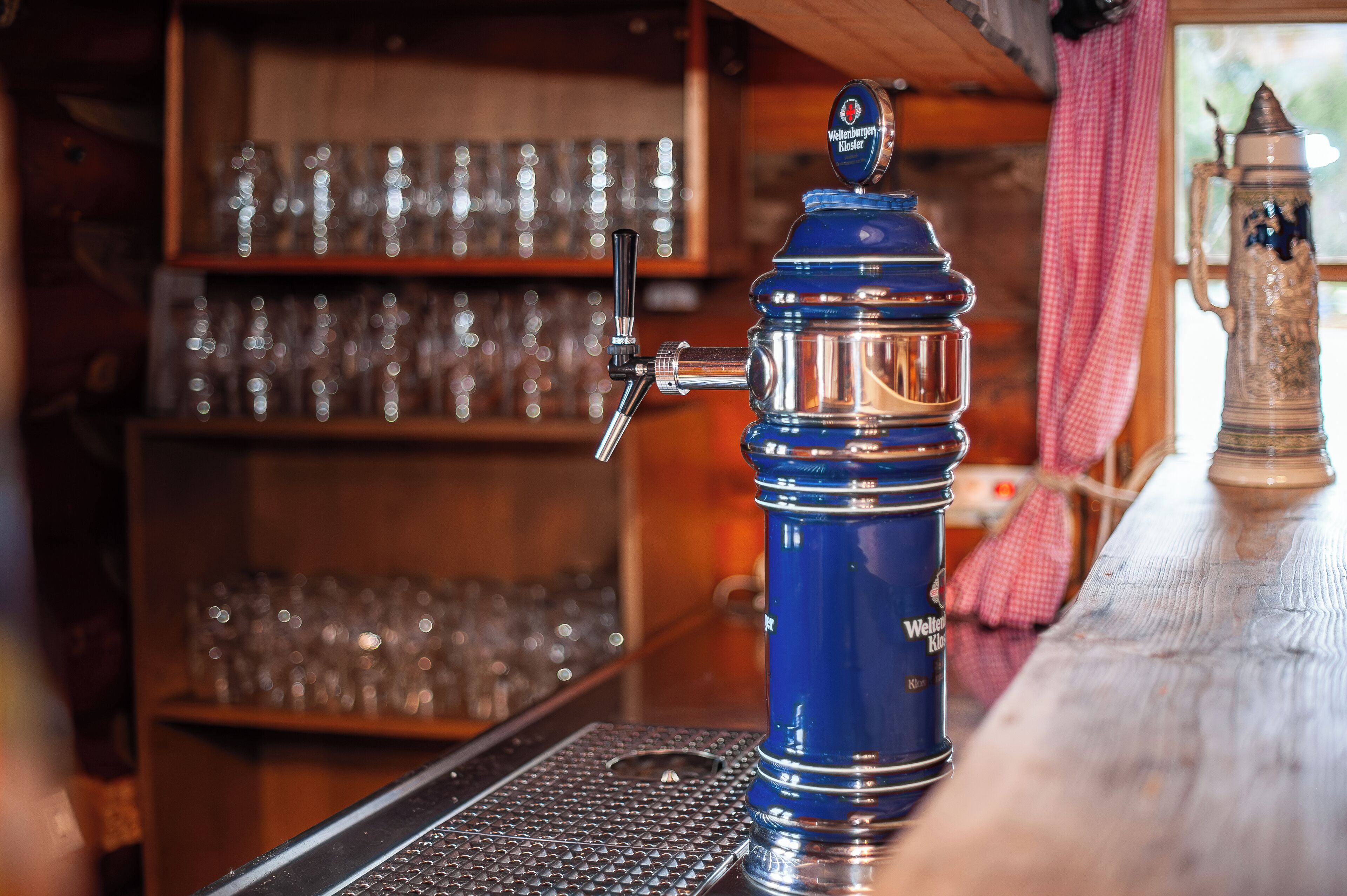 A bar area with a blue beer tap, shelves with glasses, and a rustic wooden counter.