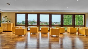 A spacious room with large windows, wooden flooring, and yellow upholstered furniture. - LuCA HOTEL (Bodenmais)