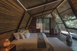 A modern, triangular-roofed bedroom with a large bed, bedside lamps, and a view of the outdoors.