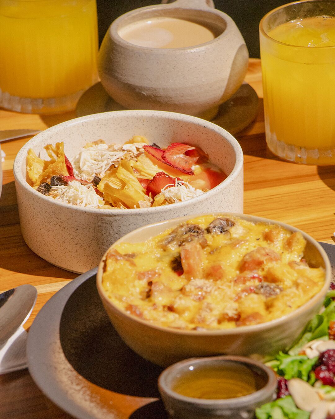 A table with a bowl of fruit salad, a bowl of scrambled eggs, and a glass of orange juice.