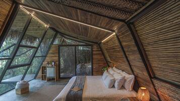 Un dormitorio con una cama grande, una mesita de noche con lámpara y vistas al exterior a través de amplios ventanales.