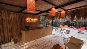 Un espace d’accueil avec un comptoir de réception en bois, des fauteuils en osier et des lampes orange suspendues.