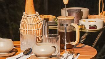 Una mesa redonda de madera con varios platos, una jarra, un jarro de cristal y una taza.