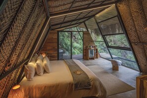 Un dormitorio acogedor y triangular con un amplio ventanal que ofrece vistas de un exuberante follaje.