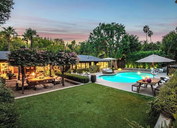 Un jardin avec une piscine, un espace salon extérieur et une pelouse bien entretenue.