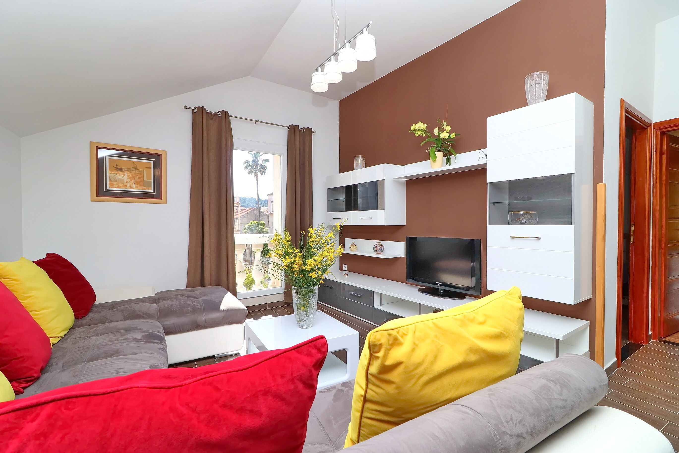 Een moderne woonkamer met een hoekbank, een flatscreen-televisie, een witte kast en een raam met gordijnen.