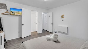 A modern hotel room with a bed, a TV mounted on the wall, a wooden floor, and a hallway leading to other rooms. - Central Bellevue Retreat  (Bellevue)