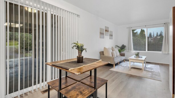 A modern living room with a wooden coffee table, a sofa, and a dining table. There are potted plants on the coffee table and a view of the outdoors through large windows. - Central Bellevue Retreat  (Bellevue)
