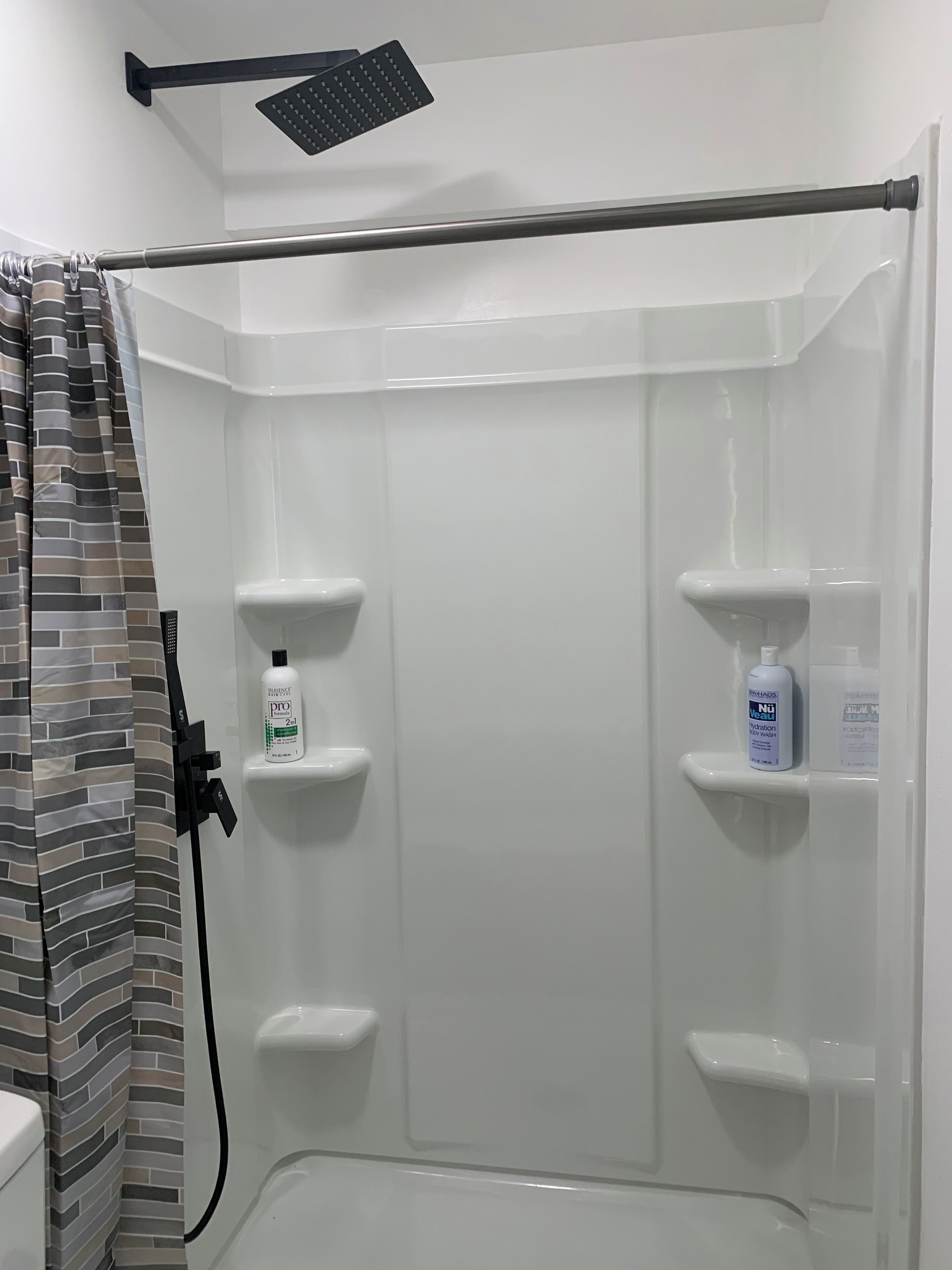 A shower area with a glass door, a showerhead, and two shelves holding toiletries.