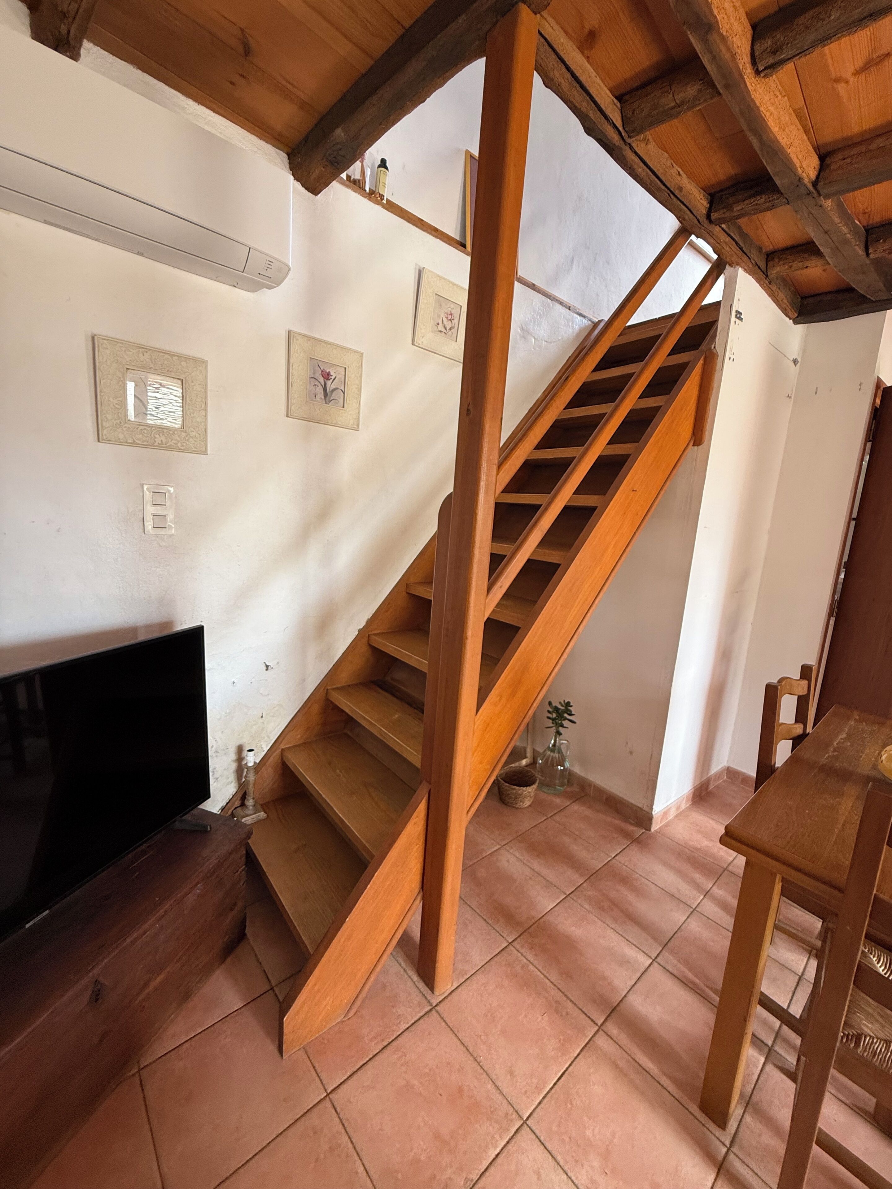 Un escalier en bois, un sol carrelé, un téléviseur à écran plat et des tableaux encadrés accrochés au mur.