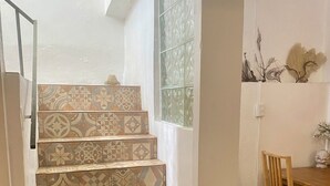 Uma escadaria com ladrilhos estampados que leva a um quarto com uma mesa de madeira e uma cadeira.