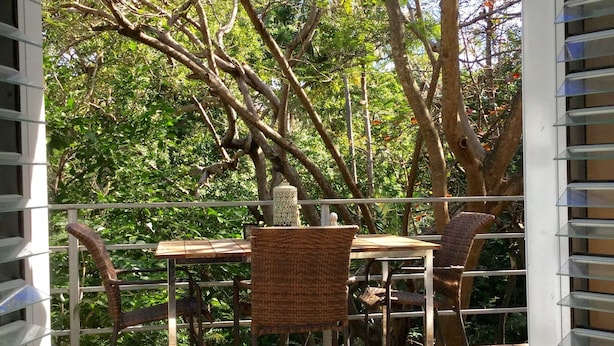 Um pátio externo com mesa e cadeiras, cercado por árvores e um deck de madeira.