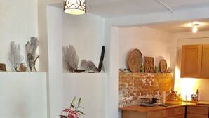 Uma sala de jantar com mesa e cadeiras de madeira, um vaso com flores, e uma cozinha com armários de madeira e painel de ladrilhos.