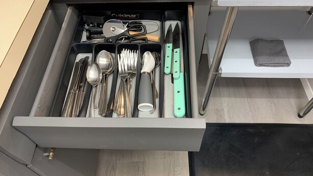 Un cajón con varios utensilios de cocina, incluyendo cucharas, tenedores, cuchillos y un rallador.