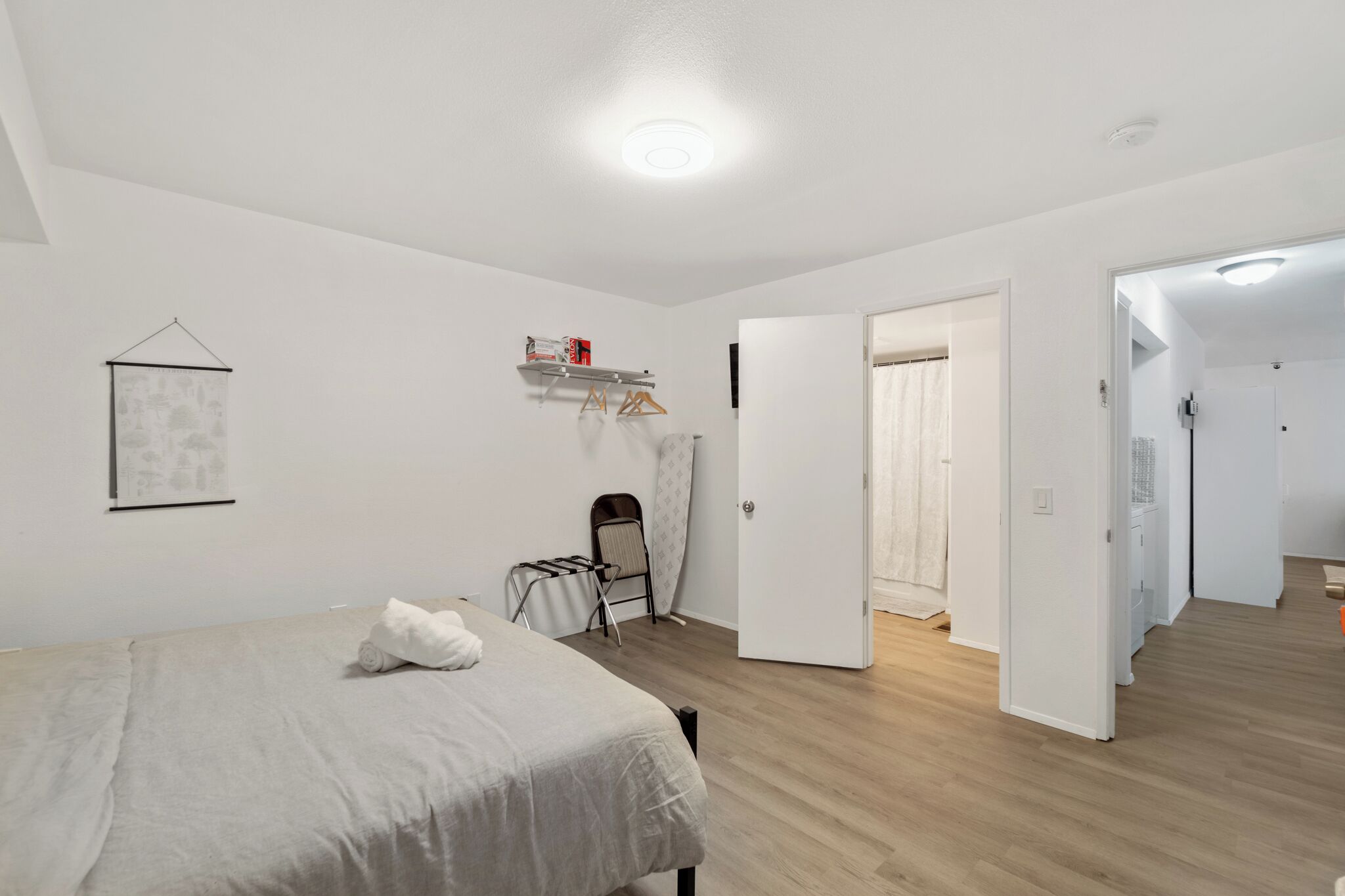 Un dormitori minimalista amb un llit, una taula petita i una cadira. Hi ha una porta que dona a una altra habitació.