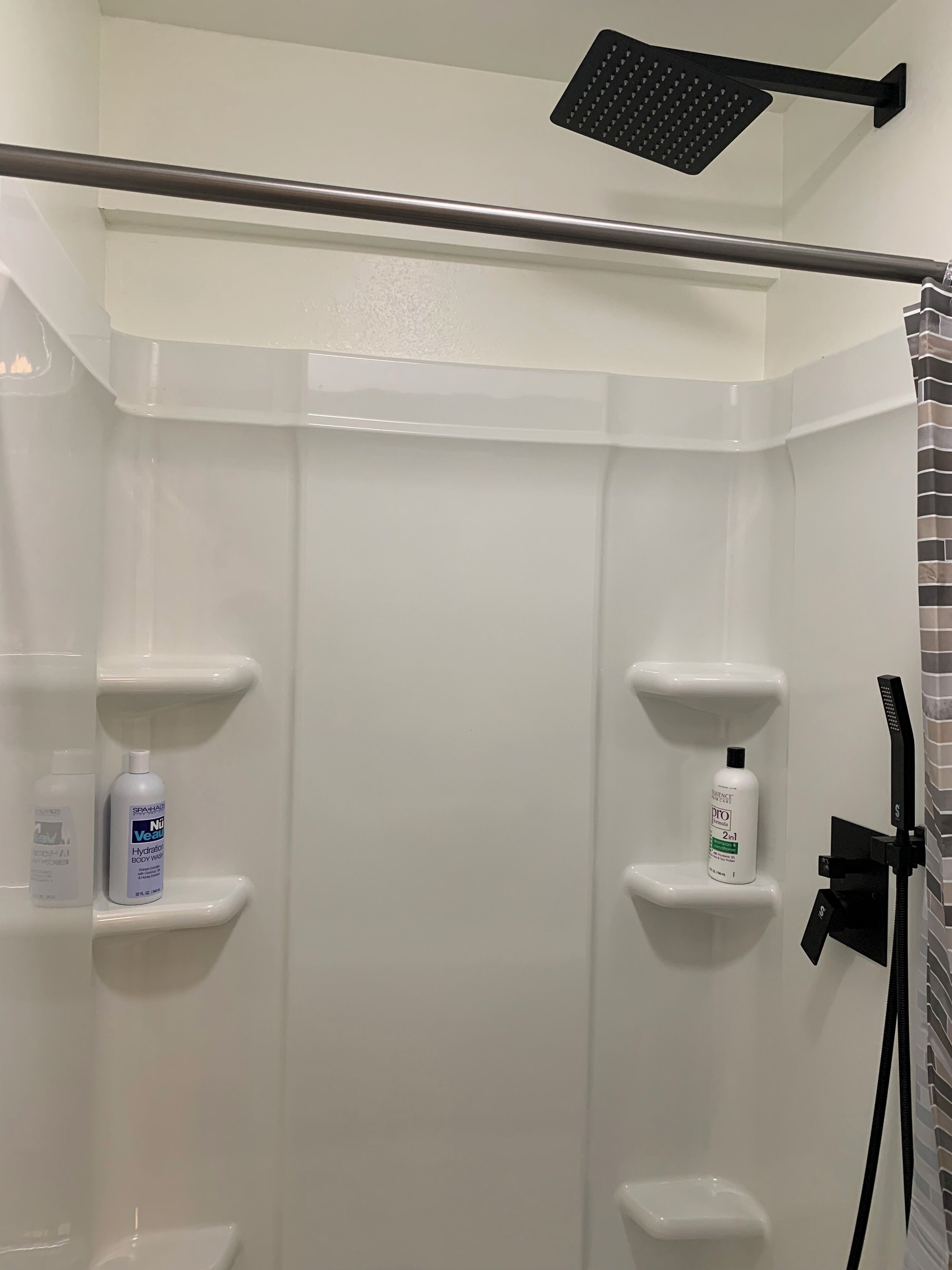 A shower area with a handheld showerhead, two white shelves with toiletries, and a black showerhead mounted on the wall.