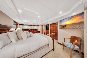 A spacious bedroom with a large bed, a wooden wardrobe, and a wall-mounted TV. - Superyacht Bahamas PrivateCruise (Tampa)