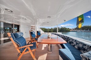 A deck with a table and chairs, a sofa, and a view of the water. - Superyacht Bahamas PrivateCruise (Tampa)